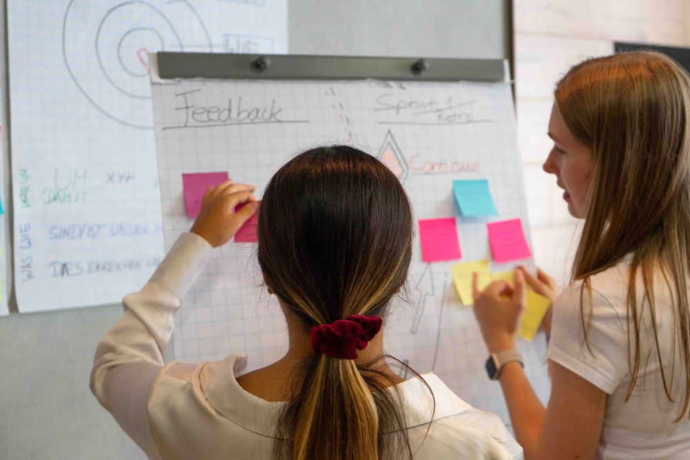 Zwei Frauen kleben bunte Post-its auf ein Flipchart während eines Workshops.