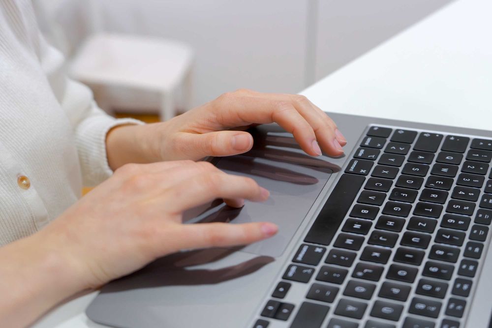 Zwei menschliche Hände tippen auf einer Computer-Tastatur in einem modernen Arbeitsumfeld.