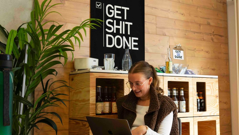 Eine Frau die am Laptop arbeitet es zu sehen im Hintergrund ist ein Büroraum.