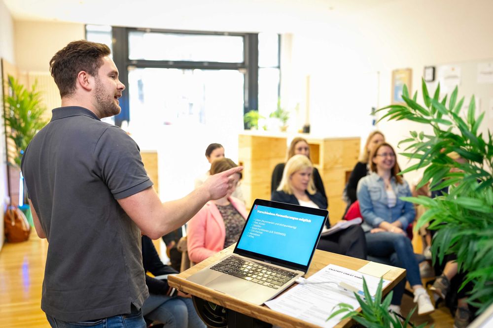 Ein Mann präsentiert Inhalte auf einem Laptop während eines KI-Kickstart-Workshops vor einer Gruppe Teilnehmender.