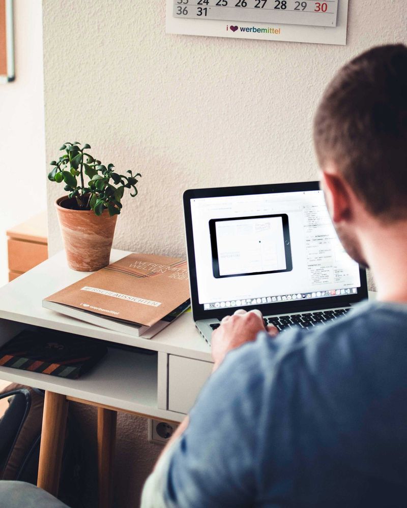 Mitarbeiter arbeitet im Büro am Laptop an einem Schreibtisch mit Pflanze und Notizbuch