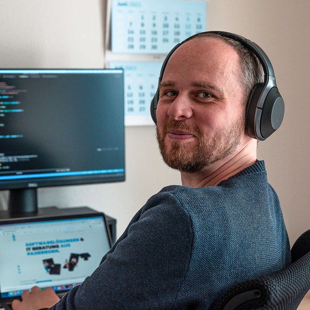 Webentwickler sitzt mit Kopfhörern am Schreibtisch und arbeitet am Computer.