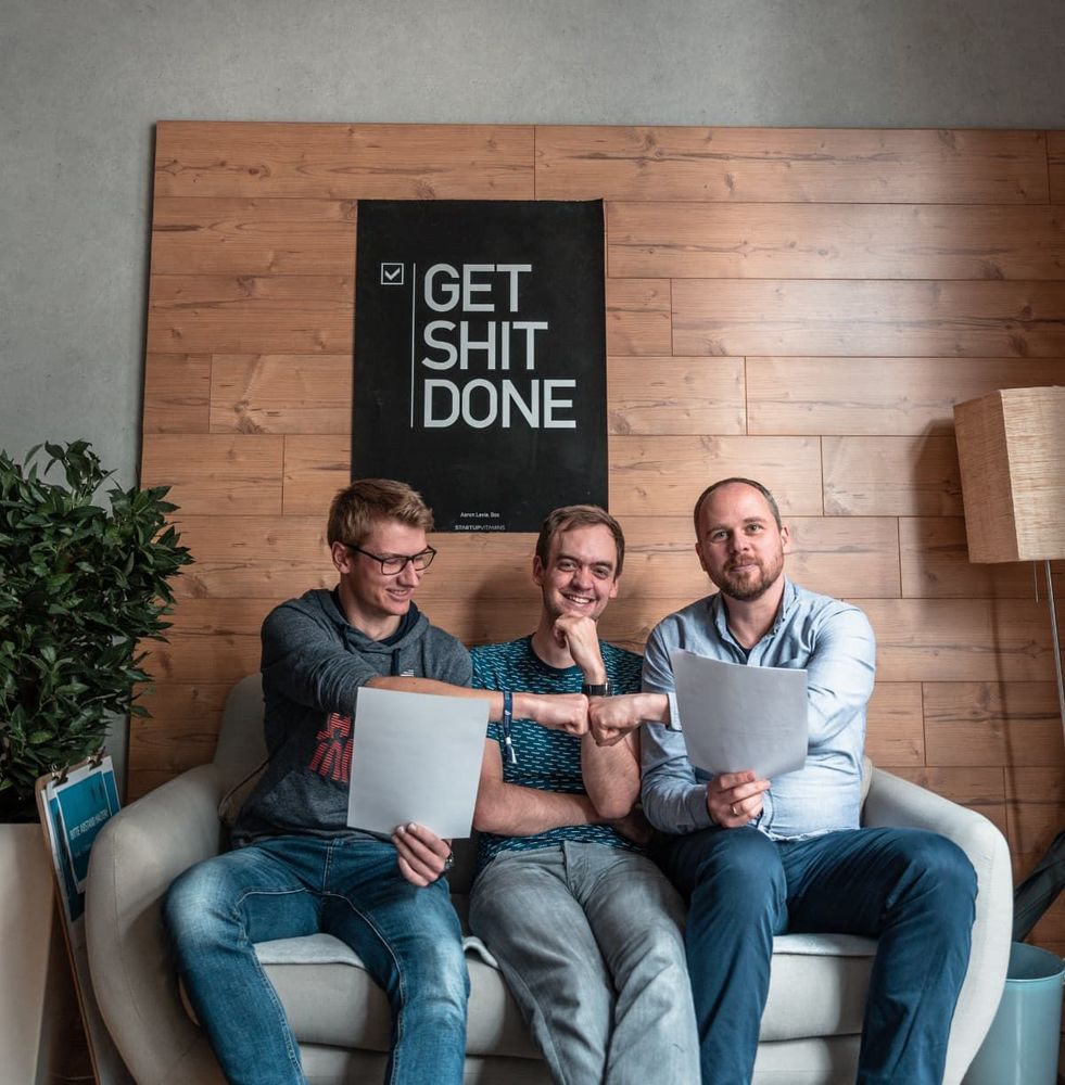 Drei enpit Mitarbeiter sitzen auf einem Sofa im enpit Büro und feiern ihre vollbrachten Leistungen